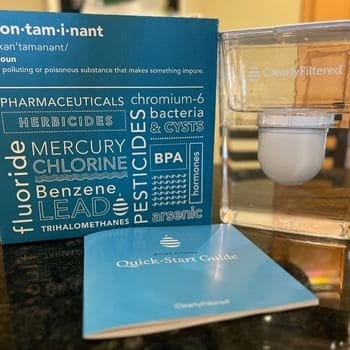 Clearly Filtered water pitcher with product box listing contaminants removed and quick-start guide on counter.