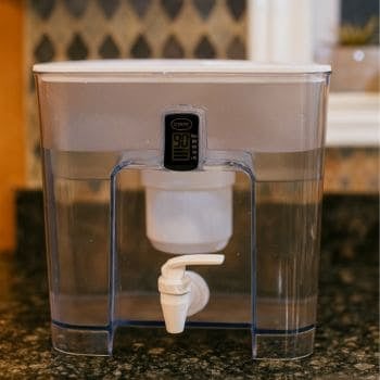 Epic Pure water filter dispenser on a dark granite kitchen countertop with digital display reads ‘START 90 Days’ with 90/60/30/<15 legend; clear reservoir and white spigot.