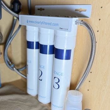 Clearly Filtered 3-Stage under-sink water filter system mounted in a kitchen cabinet with stainless steel braided hose connection