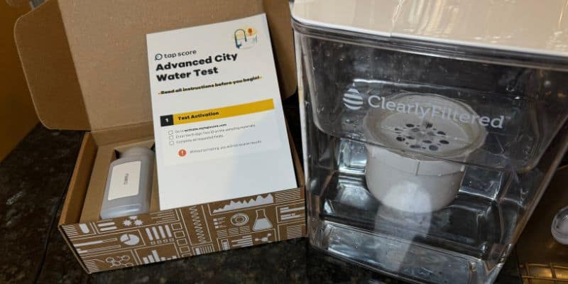 Tap Score Advanced City Water Test kit alongside the Clearly Filtered pitcher filled with water, prepared for independent lab testing.