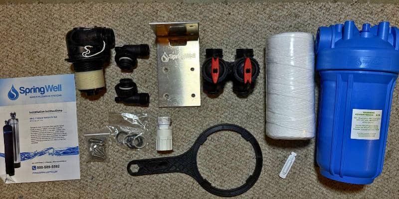 SpringWell CF1 whole house water filter installation kit laid out with housing, sediment filter, bracket, bypass parts, wrench, fittings, and instruction manual.